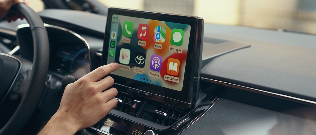 En person inne i en Toyota samhandler med bilens multimediaberøringsskjerm. Displayet viser Apple CarPlay-startskjermen.